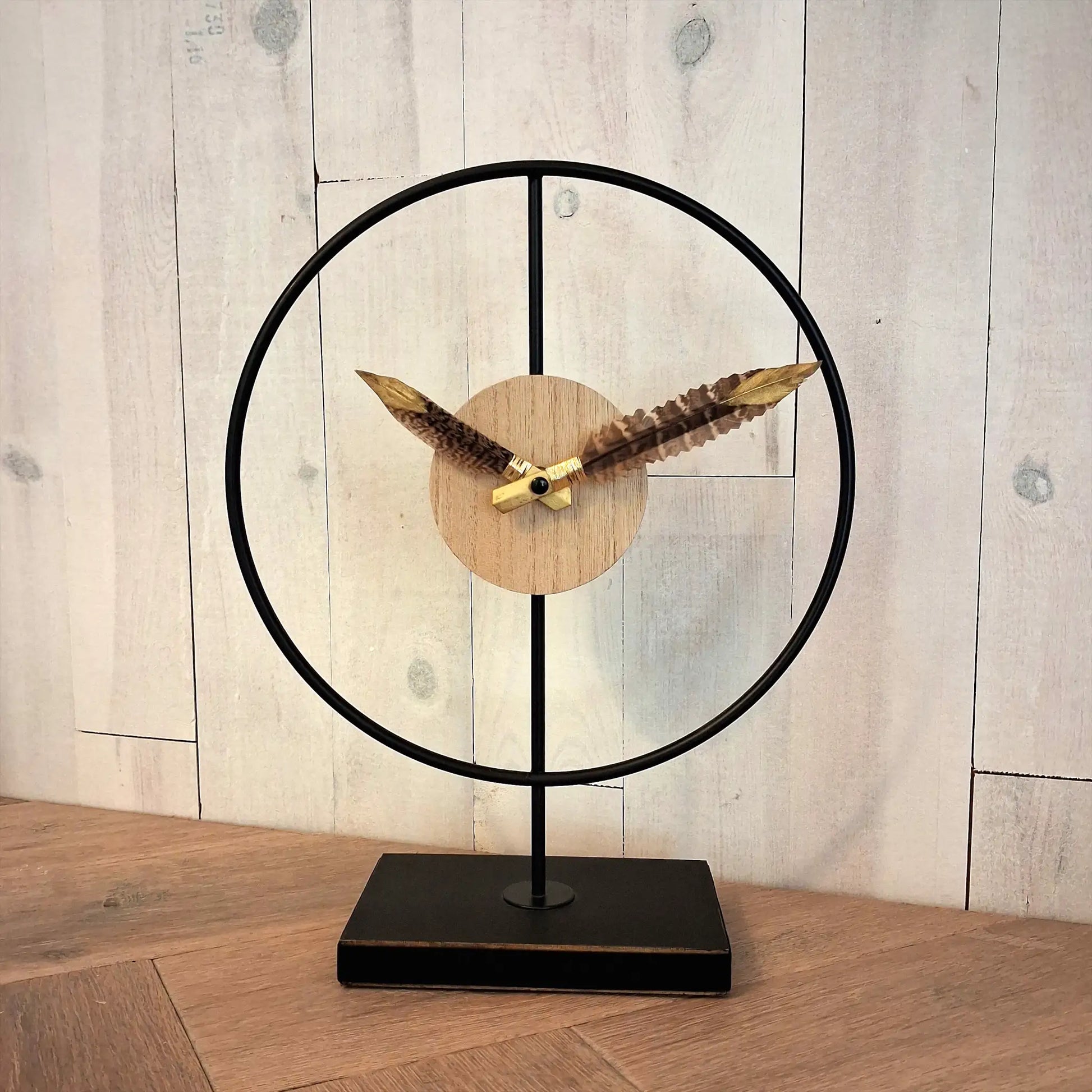 une horloge design sur pied en métal noir et bois, avec des plumes de faisan sur les aiguilles et finition dorée sur l'extrémité des plumes